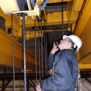 White man with a navy jacket and white hard hat inspecting an overhead bridge crane system