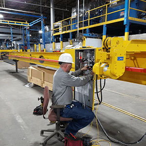 Service Crane Company employee in a long-sleeve grey shirt, white hard hat, and blue jeans performing maintenance on-site